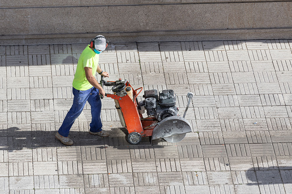 Construction worker cutting paving stone floor with diamond saw blade machine on a sidewalk